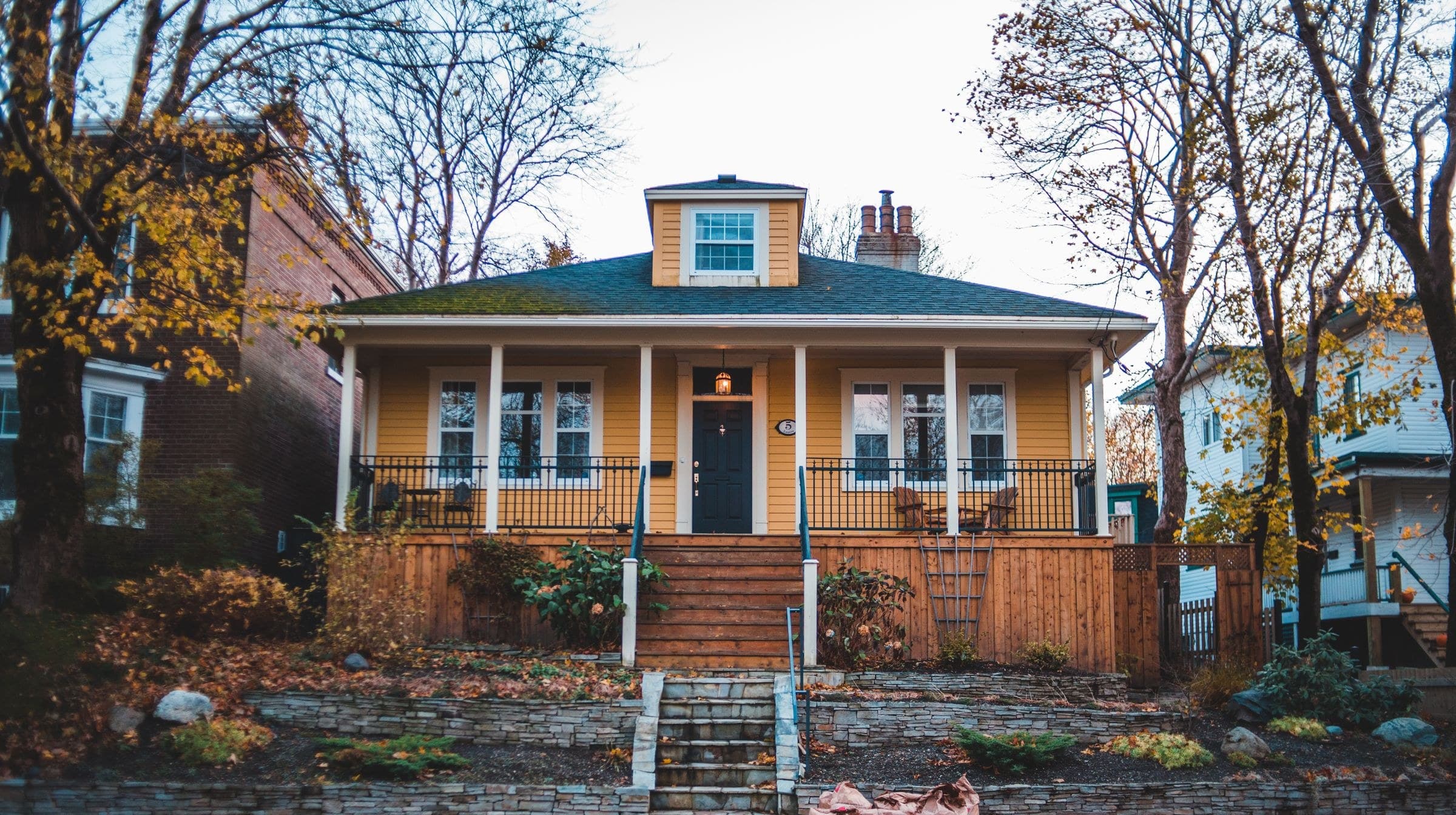 Yellow bungalow with a deep front porch and stone retaining wall in autumn