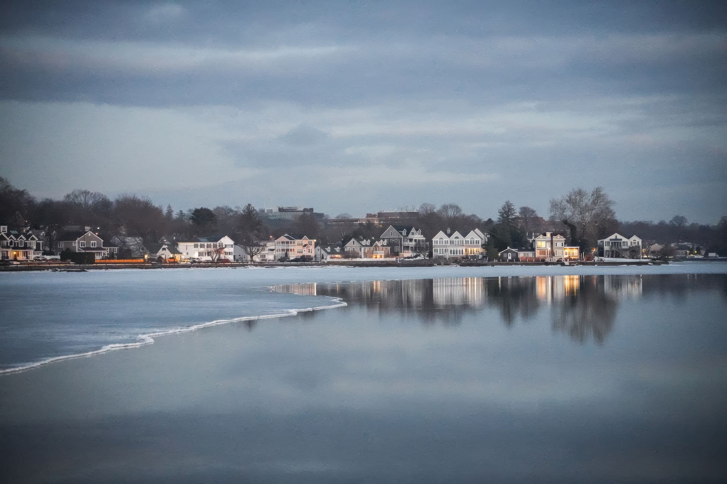 Lakefront houses reflected in calm water at dusk