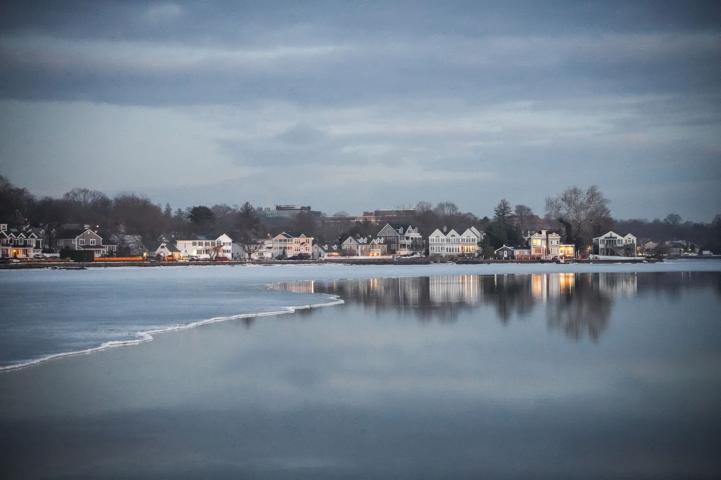 Lakefront houses reflected in calm water at dusk