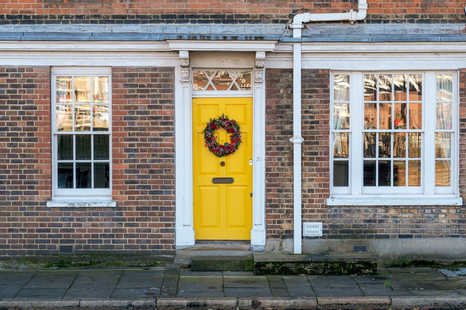 Yellow front door with a fanlight between white sash windows on a brick house