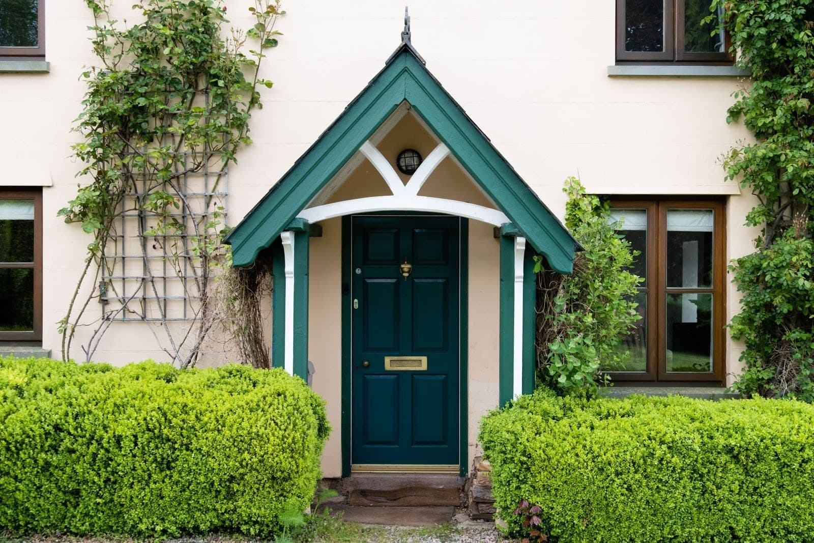 Green front door under a small gabled porch between box hedges