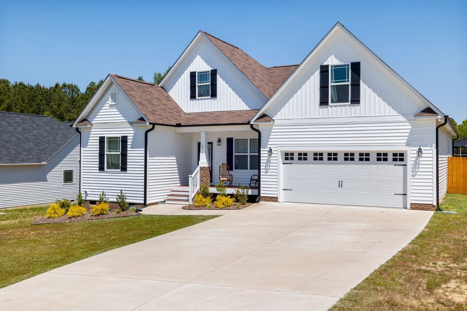 White sided house with dormers, black shutters and a double garage