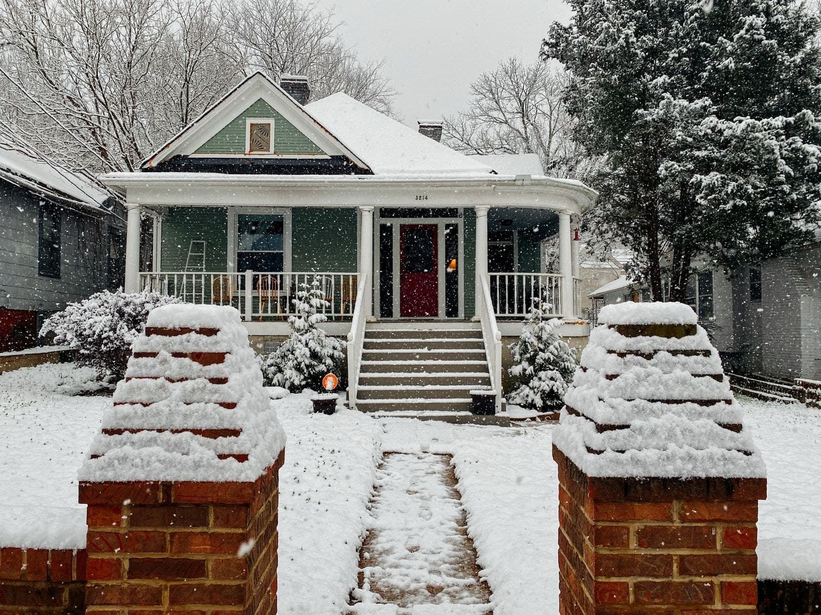 Craftsman bungalow with a porch behind snow-capped brick gate posts