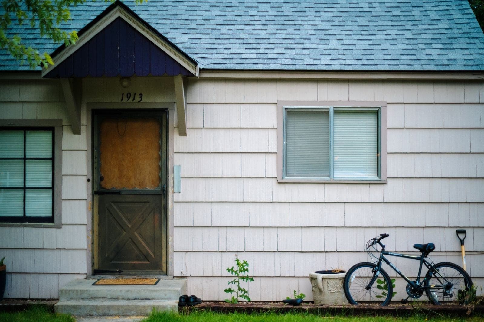 Shingled cottage with a worn wood front door and a bike against the wall