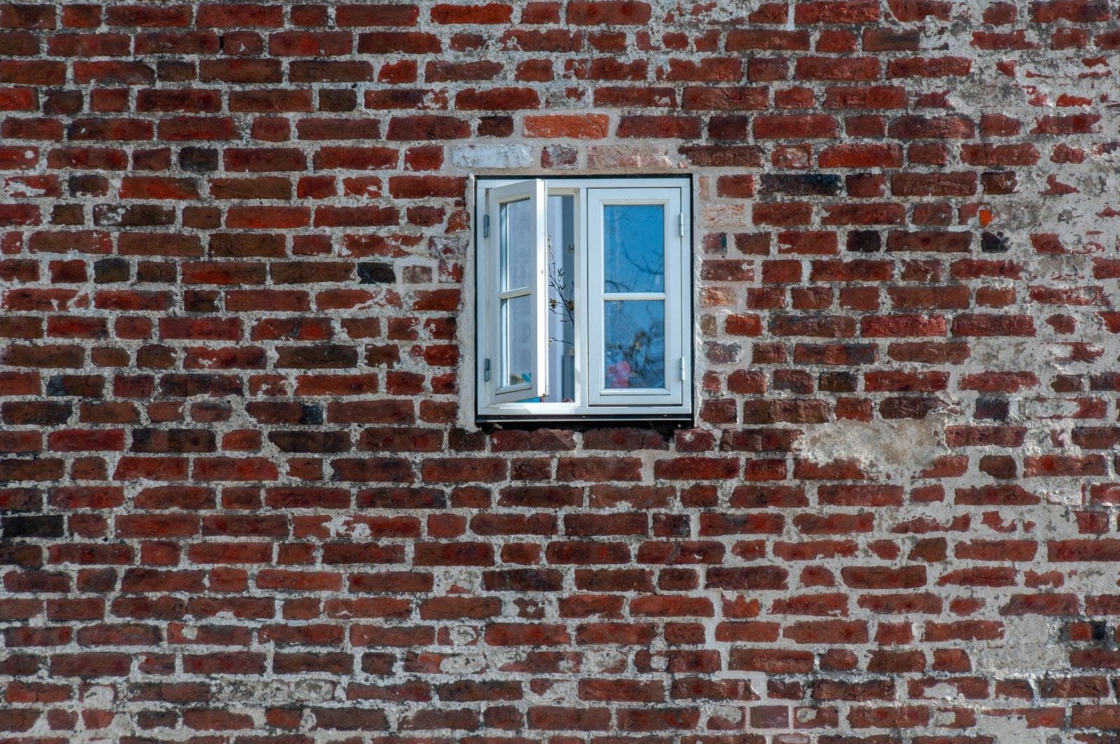 White casement window set in a weathered red brick wall