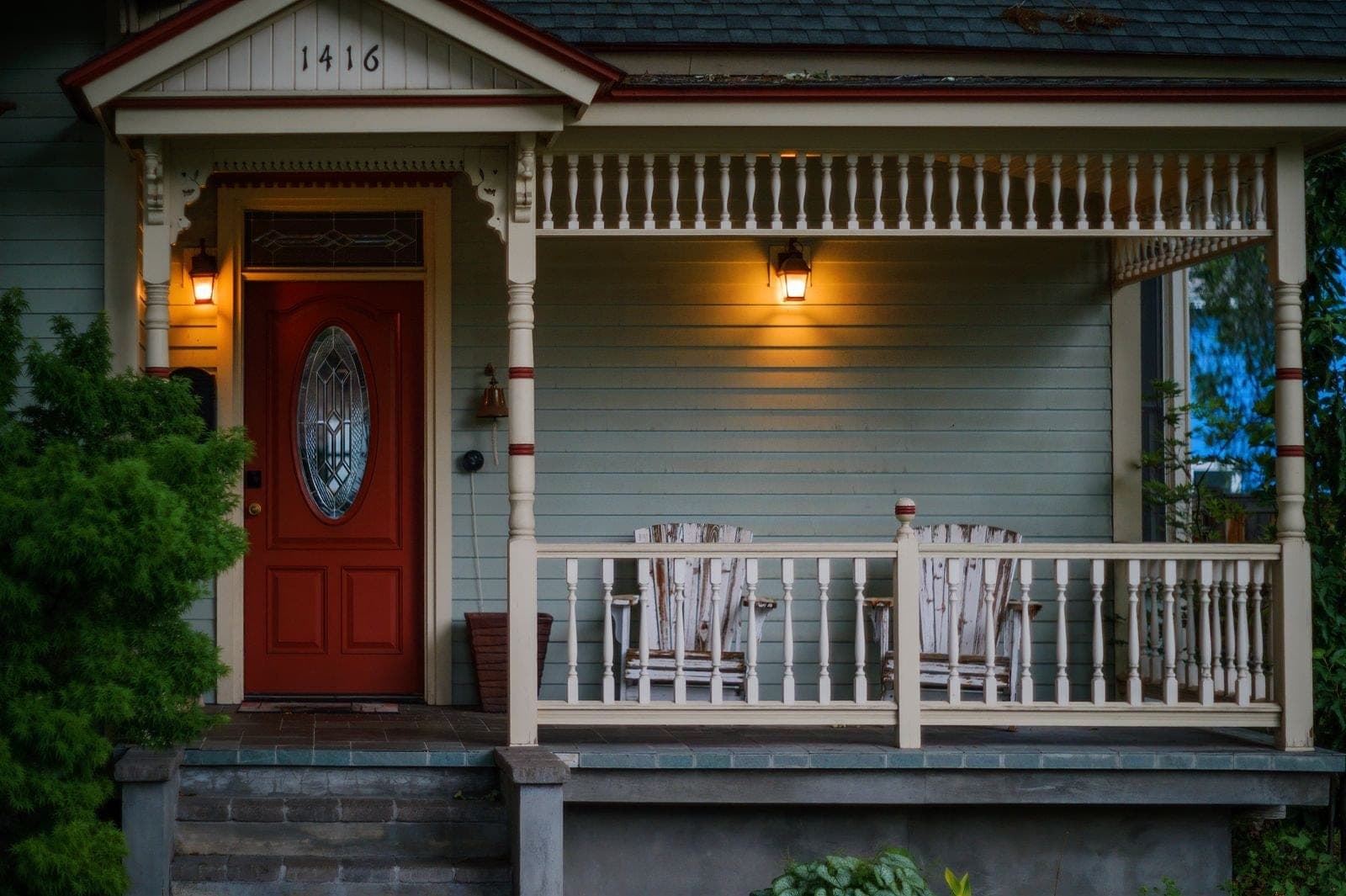 Victorian porch with a red front door, oval glass and spindle railings