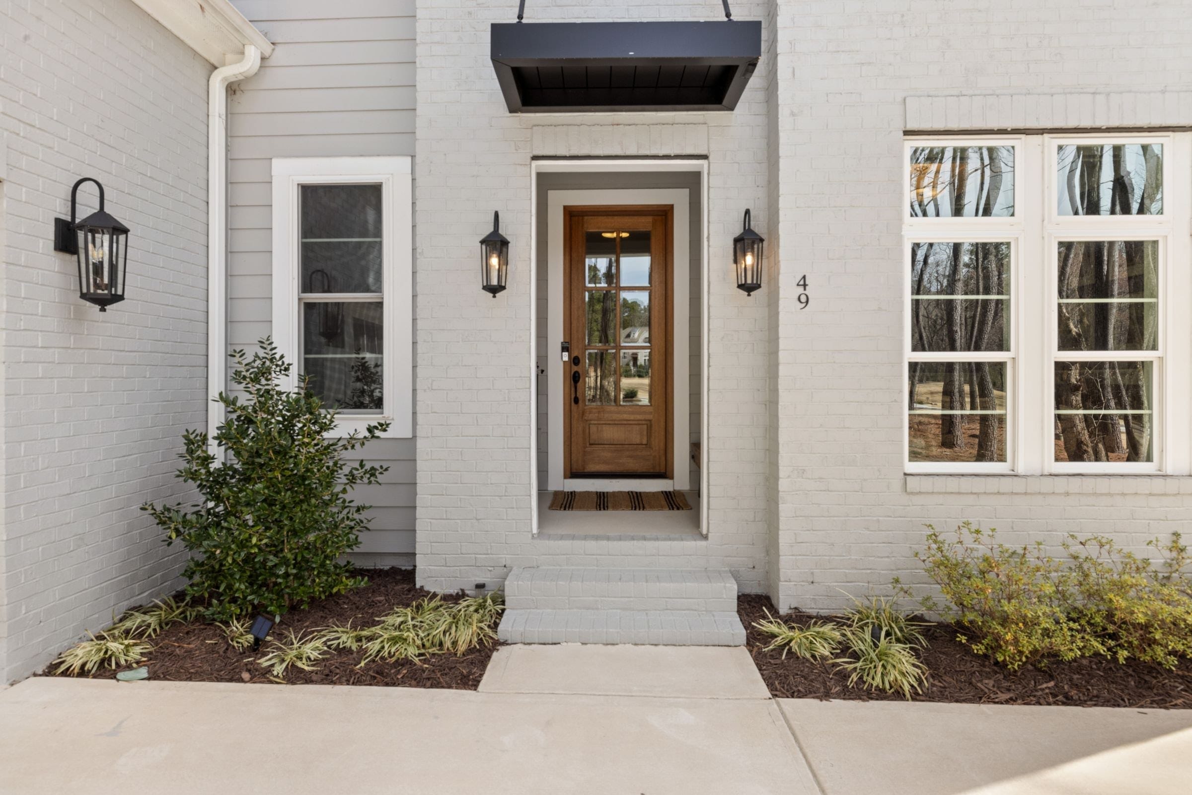 Wood-look front entry door with glass panes and wall lanterns on a white brick house
